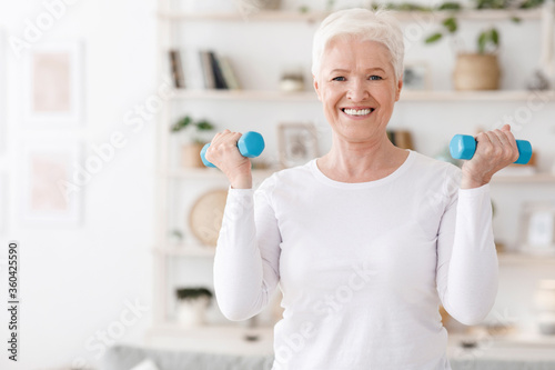 Healthy Lifestyle. Positive elderly woman training with dumbbells at home