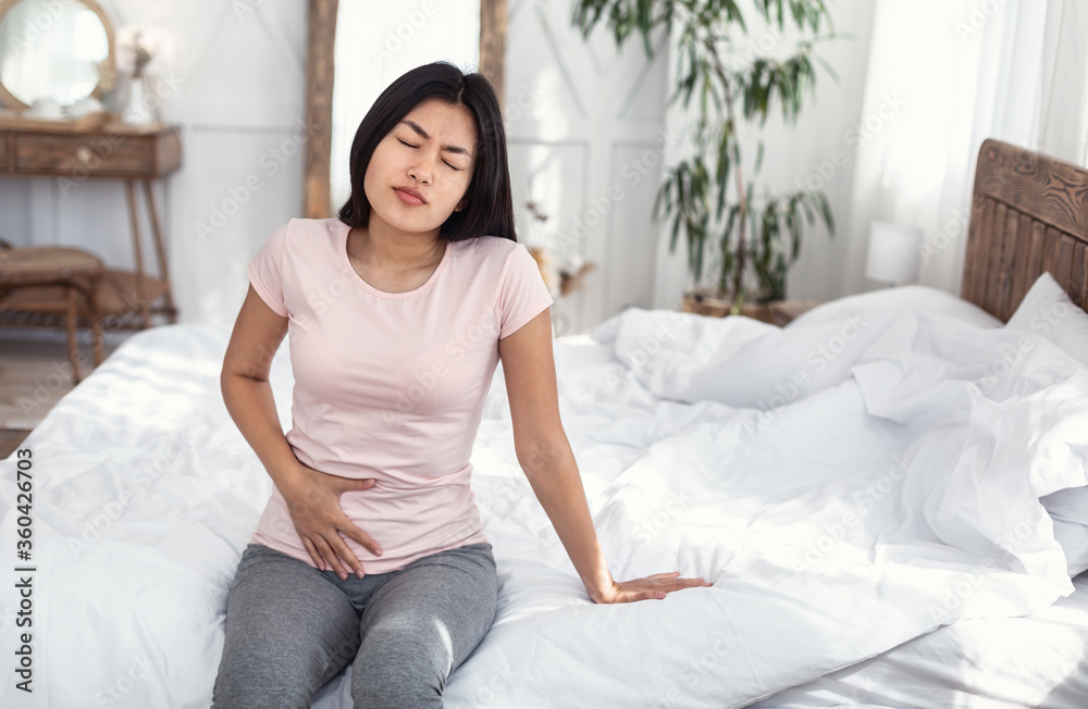 Japanese Girl Touching Aching Lower Abdomen Sitting On Bed Indoors Japanese Girl Touching Aching Lower Abdomen Sitting On Bed Indoors