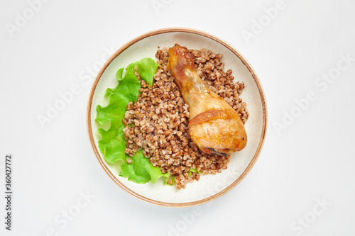Buckwheat with fried chicken leg on a white plate with a green leaf of salad. Russian traditional cuisine. White background.
