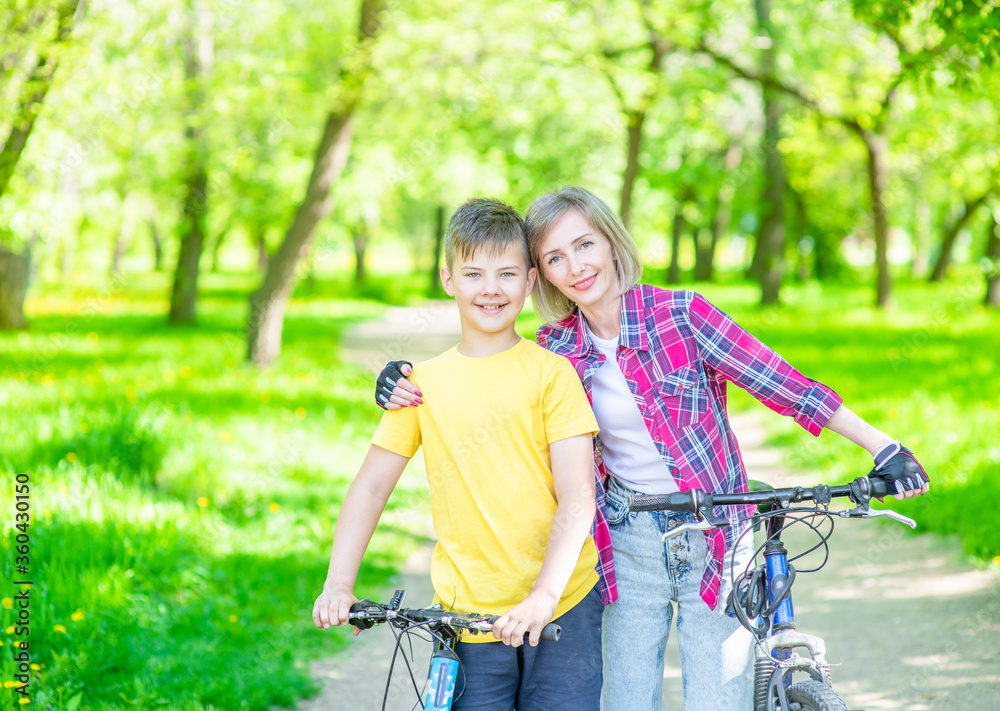 Happy family. Smiling mother embraces her young son, who ride bikes in a summer park. Empty space for text Happy family. Smiling mother embraces her young son, who ride bikes in a summer park. Empty space for text