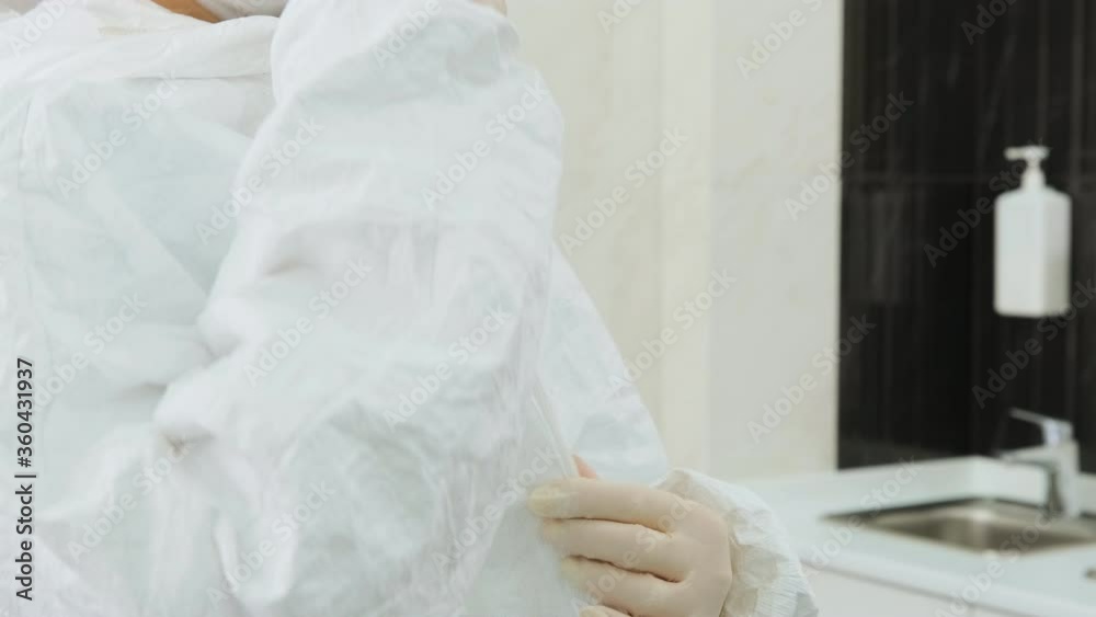 The doctor wears a white protective suit in the clinic or hospital and zips up the gown. Dentist prepares to receive patients during coronavirus pandemic.