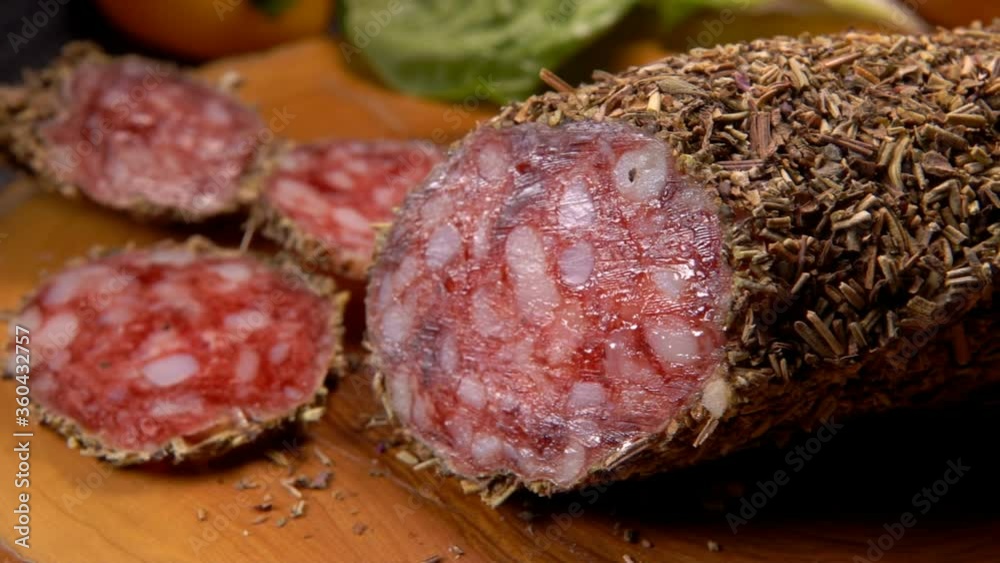 Panorama of delicious dry sausage in herbs cut into slices on a wooden board on the background of greenery Panorama of delicious dry sausage in herbs cut into slices on a wooden board on the background of greenery