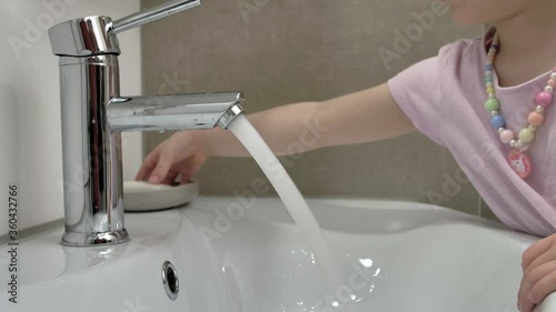 A little girl with beads and bracelet carefully washes her hands with soap under the tap