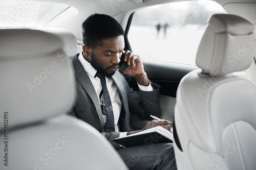 Busy Businessman Talking On Phone Taking Notes Sitting In Car © Prostock-studio