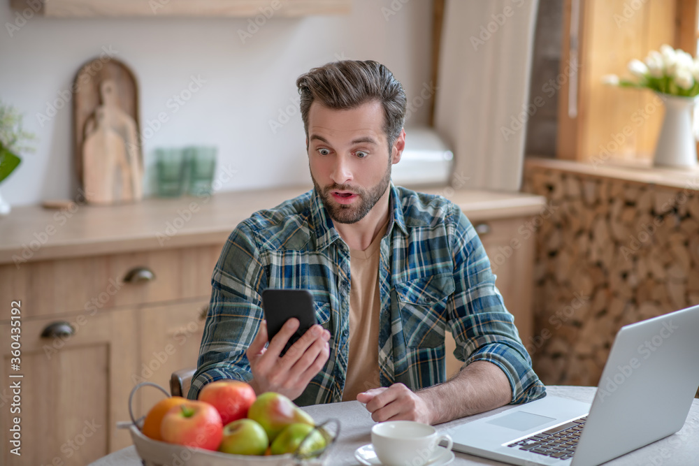 Man in a checkered shirt reading a message and looking astonished Man in a checkered shirt reading a message and looking astonished