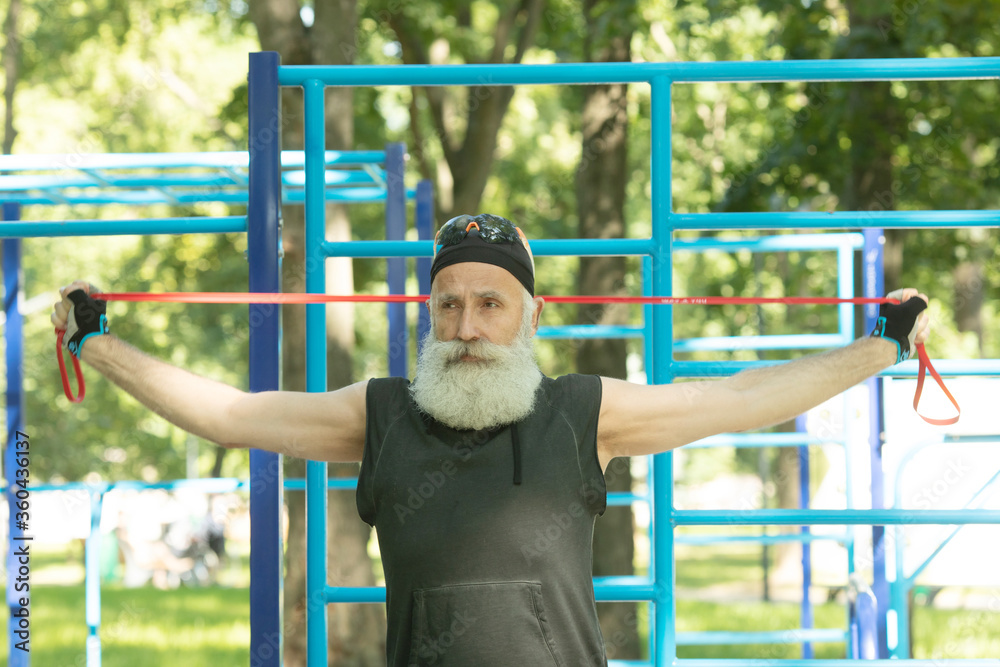 Obraz premium Old man doing fitness exercises with elastic resistance band.Bearded senior training with rubber band. Workout ,sports, healthy lifestyle concept.