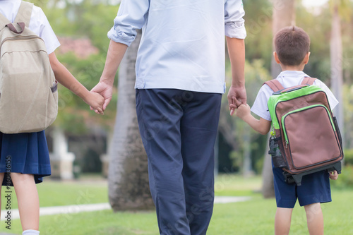 Asian young father holding hand his son and daughter walking to school in the morning
