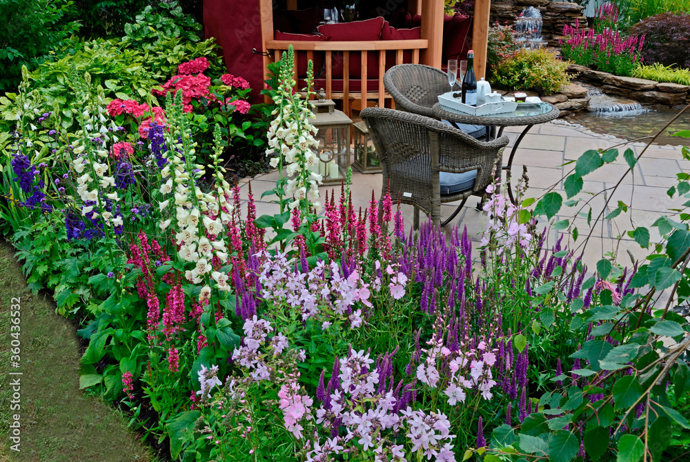The patio area of an aquatic garden with colourful flower border with Summer House and outdoor eating on the terrace