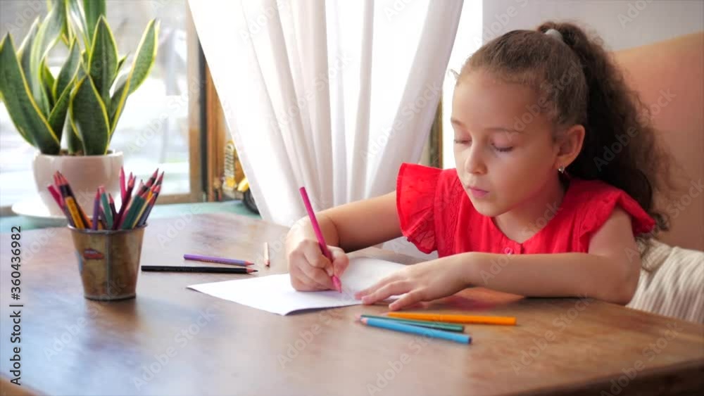 Happy Little Girl or Cute primary child school child of 7-8 years old at home relaxing sits in house and paints on paper use colour pencils. Child draws,focused children elementary education concept. Happy Little Girl or Cute primary child school child of 7-8 years old at home relaxing sits in house and paints on paper use colour pencils. Child draws,focused children elementary education concept.