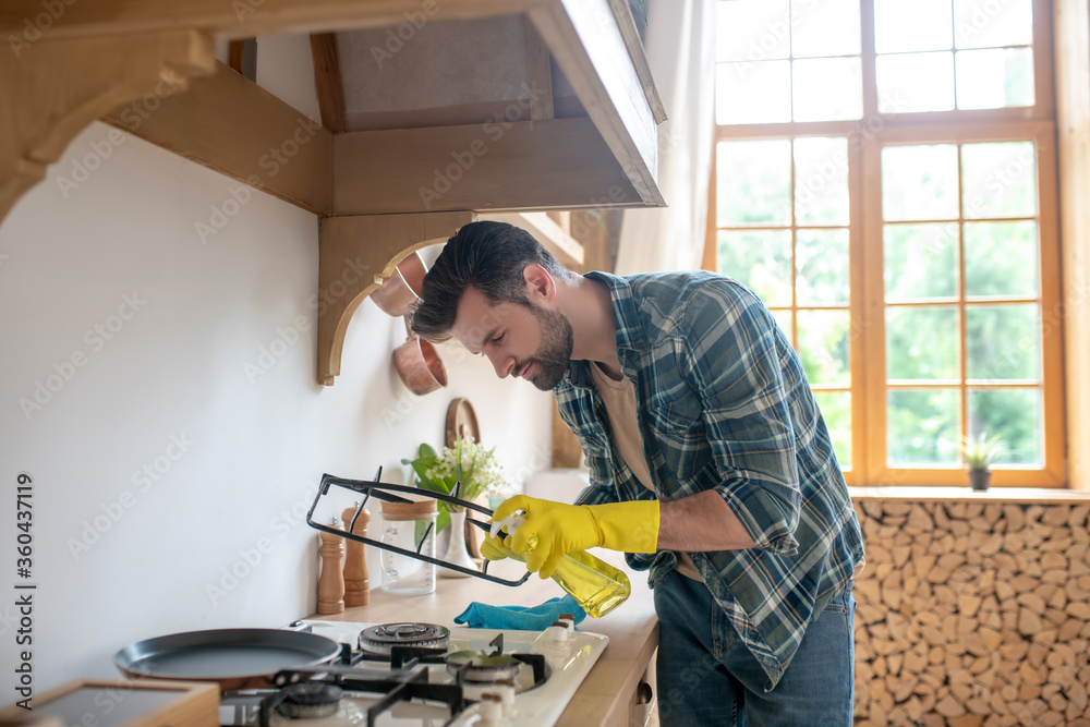 Dark-haired man in yellow gloves sitting and cleaning the oven in the kitchen Dark-haired man in yellow gloves sitting and cleaning the oven in the kitchen