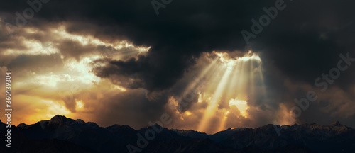 Obraz na plátně Rays of light shining through dark clouds over mountains