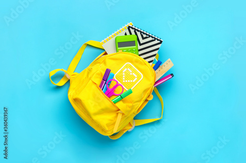 Back to school, education concept. Yellow backpack with school supplies - notebook, pens, ruler, calculator, scissors isolated on blue background. Top view. Copy space Flat lay composition Banner