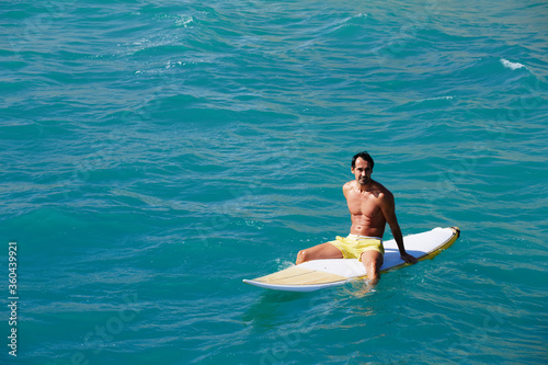 Shot of a handsome young man enjoying a surf in clear blue water, male surfer in the ocean water with surf board, sexy man surfing at the beach, men drifting on surfboard in the copy space ocean