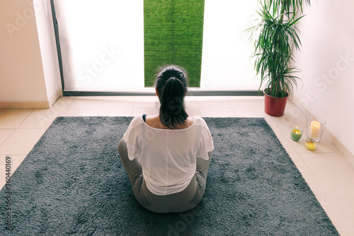 Woman sitting on the floor relaxing and looking out the window, doing meditation exercises at home