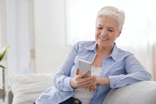 Modern Technologies For Seniors. Smiling Elderly Lady Using Smartphone At Home