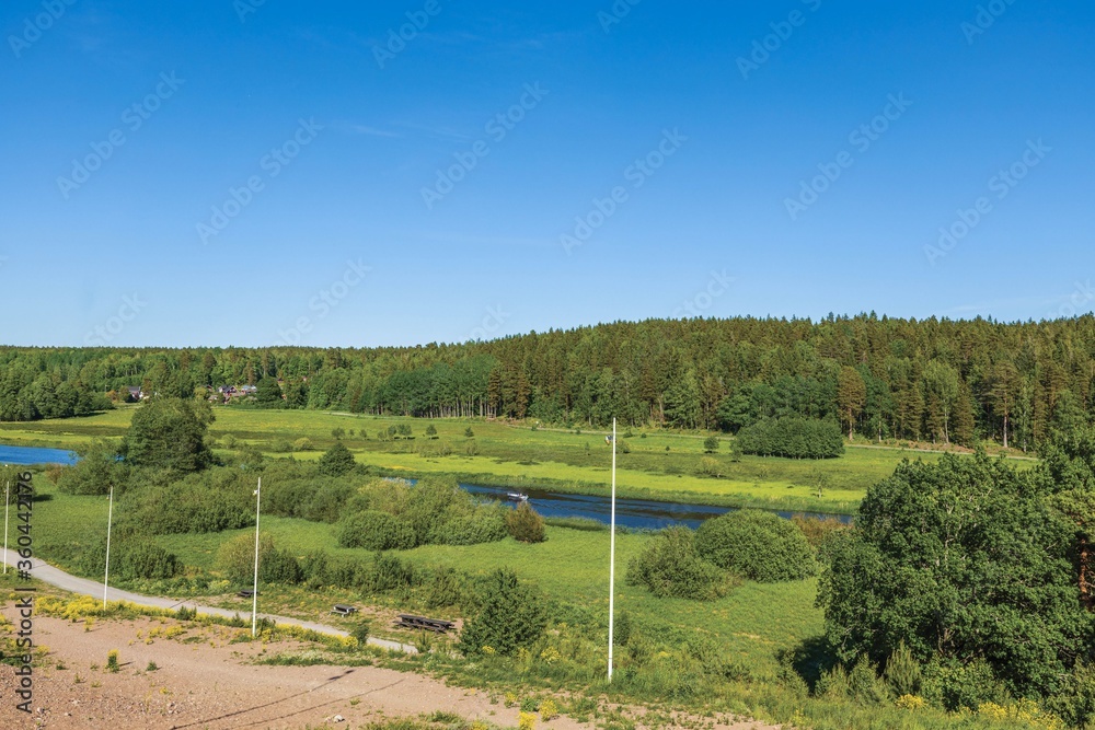 Gorgeous nature landscape view. Traditional private wooden houses between green forest trees. Small river along asphalt road. Sweden. 