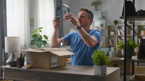 Handsome young man pulls out headphones from a cardboard box. Unpacking online purchases.