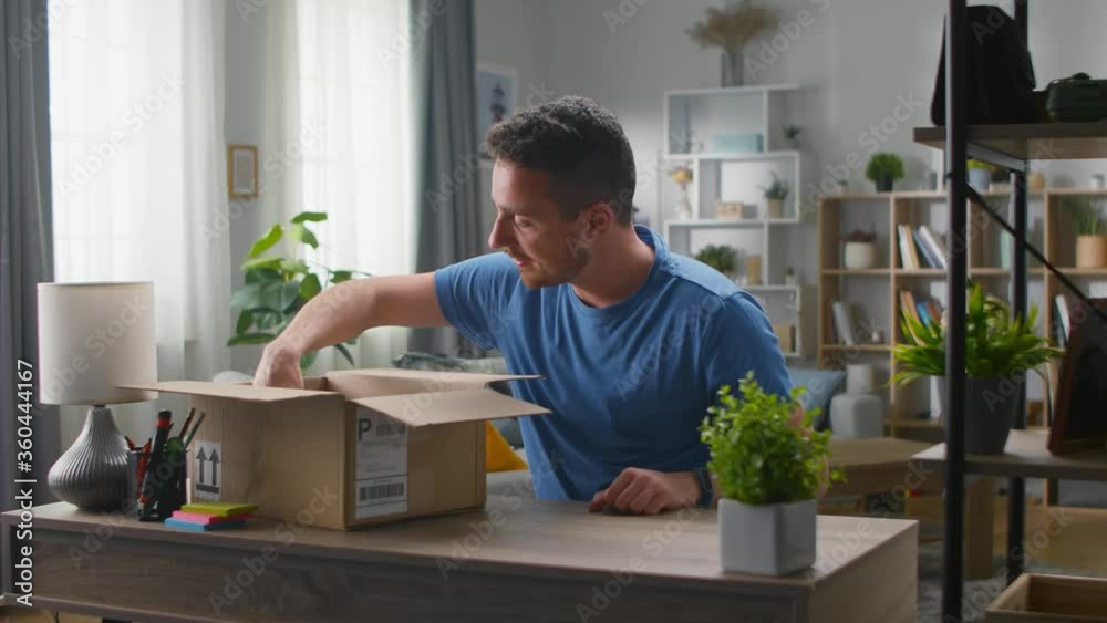 Handsome young man gets poverbank from the carton. Unpacking online purchases. Handsome young man gets poverbank from the carton. Unpacking online purchases.