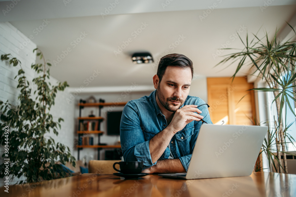 © bnenin - Portrait of a casual entrepreneur looking at laptop at home office.