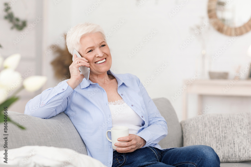 Cheerful senior woman talking on mobile phone and enjoying coffee at home Cheerful senior woman talking on mobile phone and enjoying coffee at home