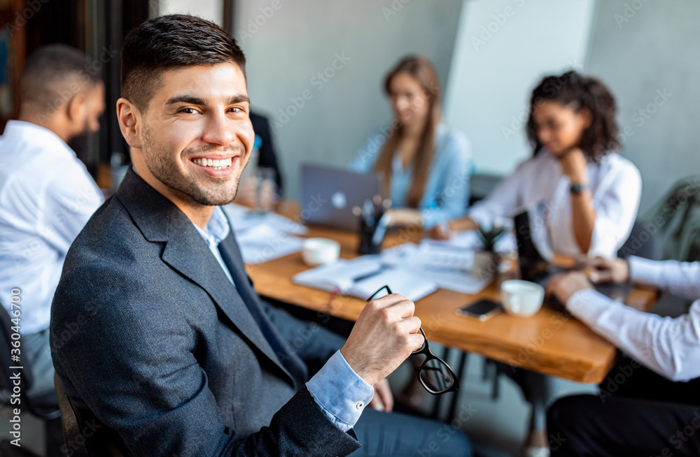 Businessman Smiling To Camera Sitting With Business Partners In Office Businessman Smiling To Camera Sitting With Business Partners In Office