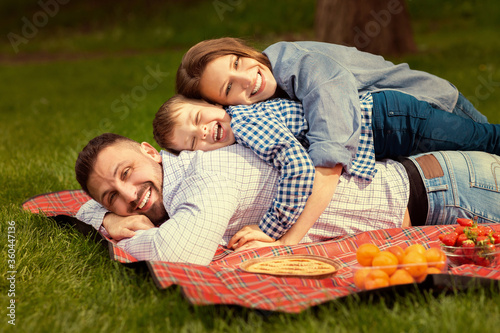 Millennial family with happy son hugging on picnic blanket in countryside
