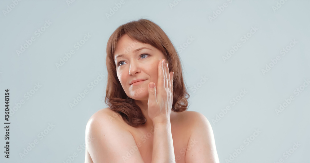 Pretty mature female applies skin care product by touching face with hand. Woman applying anti-age cream on her skin isolated on white background. Spa and wellness concept. Pretty mature female applies skin care product by touching face with hand. Woman applying anti-age cream on her skin isolated on white background. Spa and wellness concept.
