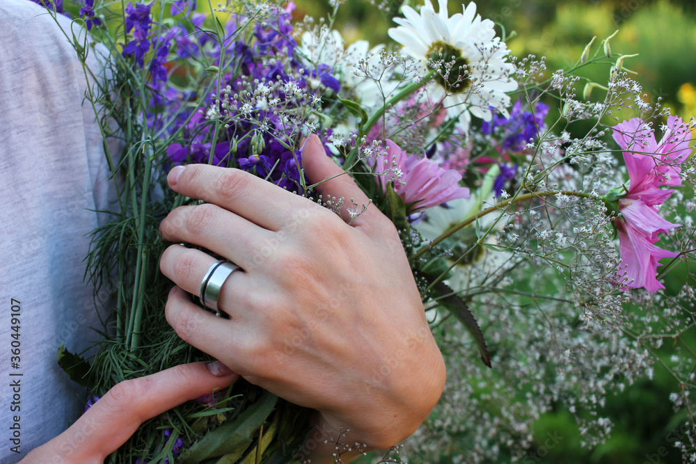 Fototapeta premium Woman's hands with summer flowers. Bouquet of daisies and echinacea in a hand.