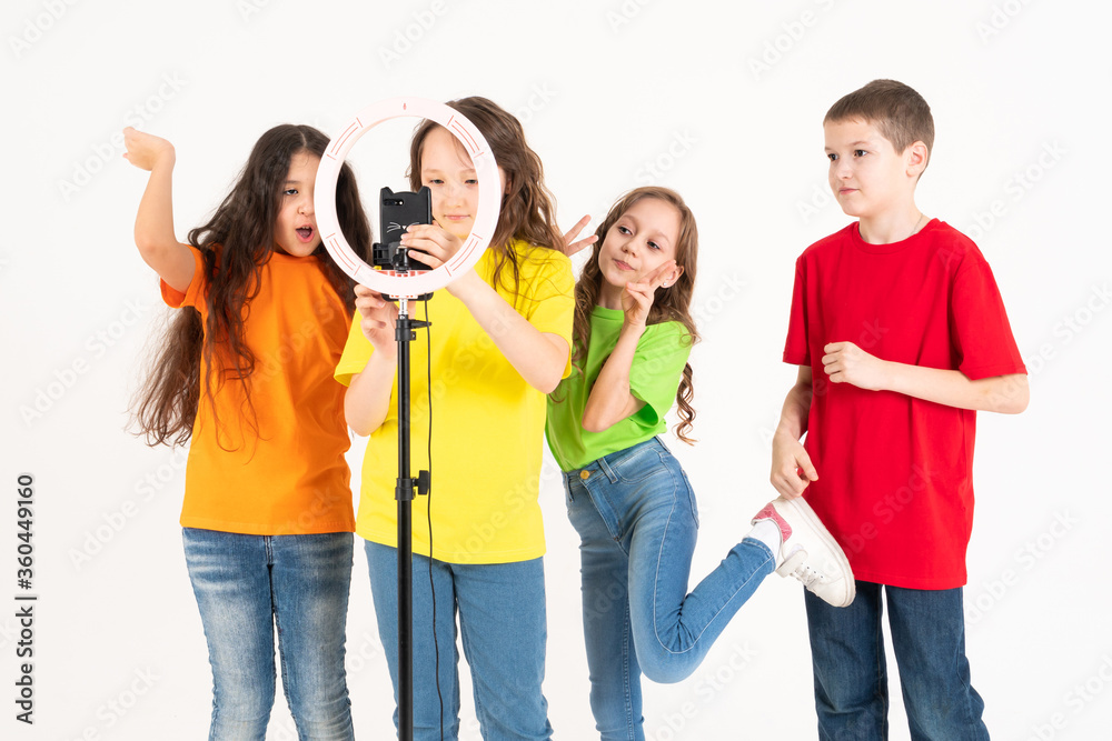 Obraz premium A group of children bloggers shoot video on the phone. Selfies The phone is mounted on a modern round lamp with a tripod.