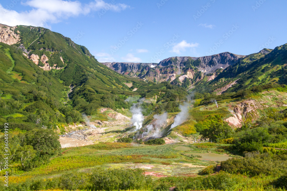 Fototapeta premium Daytime view in clear sunny weather of the valley of geysers. Mountains and volcanoes are visible on the horizon.