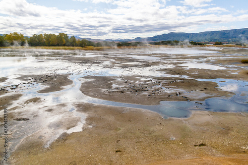 Daytime view in clear sunny weather of the valley of geysers. Mountains and volcanoes are visible on the horizon.