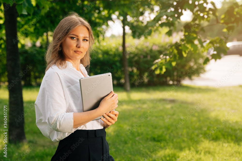 Portrait of a confident business girl looking at the camera. Businesswoman holds digital tablet in hand, stern look Portrait of a confident business girl looking at the camera. Businesswoman holds digital tablet in hand, stern look