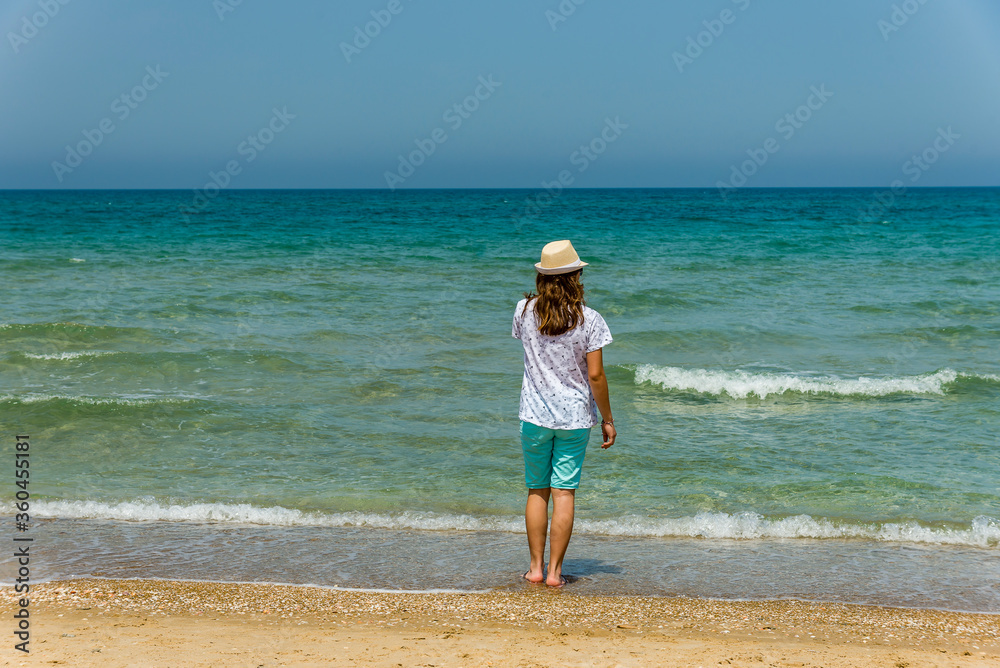Teenage girl standing on the beach looking backwards