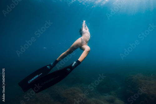 Sporty woman freediver with fins glides underwater in blue sea.