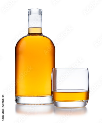 A full bell shaped bottle of golden whisky, with no label or branding, and a glass of whisky, isolated on white