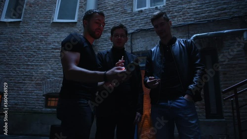 Three male friends stands outside the bar. Having conversation. In nice clothes.