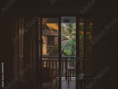 View from a hotel room on the palms outside through a slightly opened balcony glass door.