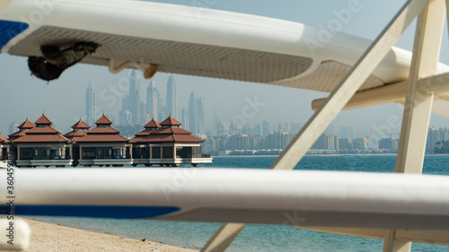 Bungalow's standing on the water with the Dubai skyline on the background and surf boards on the foreground.