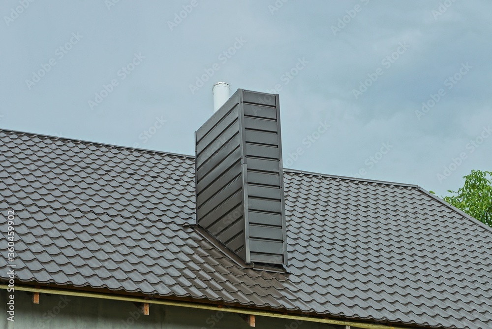 one large metal chimney on a brown tiled roof of a house against a blue sky