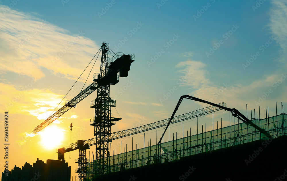 Cranes are silhouetted at a construction site at sunset