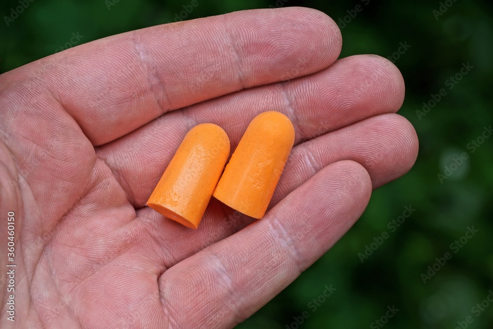 two orange plastic earplugs lie on a palm on a green background two orange plastic earplugs lie on a palm on a green background