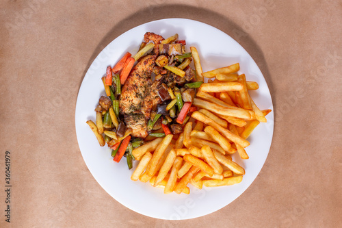 A nice plate of roasted chicken, seasoned with herbs, pepper, salt, oregano, and garlic. Also accompanied by vegetables fried on olive oil. Accompanied by French fries on a white plate.