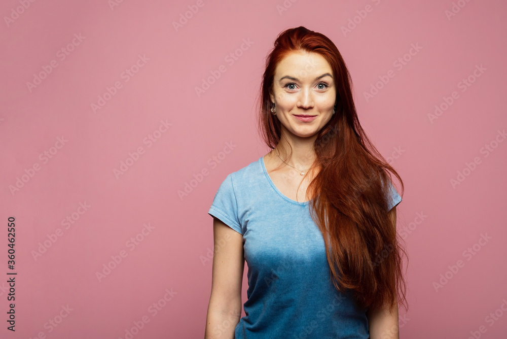 An attractive girl with red head is on the pink background. A girl is smiling on the background. An attractive girl with red head is on the pink background. A girl is smiling on the background.