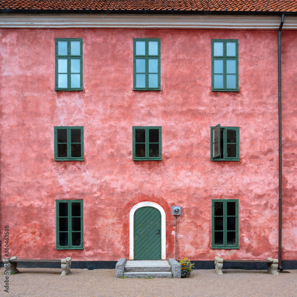An old pink facade with green windows and a green door in full symmetry