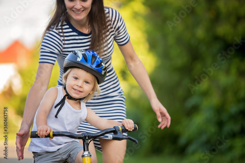 Young mother, helping her son to learn how to ride a bike, holding him and teaching him © Tomsickova