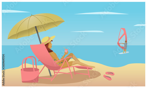 girl on the beach under an umbrella lying in a chaise longue and looking at the windsurfer