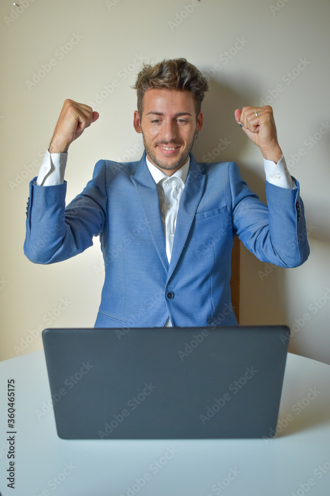 Man in a suit sitting in front of a computer, raising his arms for happiness, success Man in a suit sitting in front of a computer, raising his arms for happiness, success