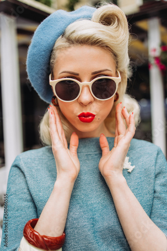 Beautiful girl model blonde sitting on a barrel in a cafe in retro style with a beret and in an interesting image