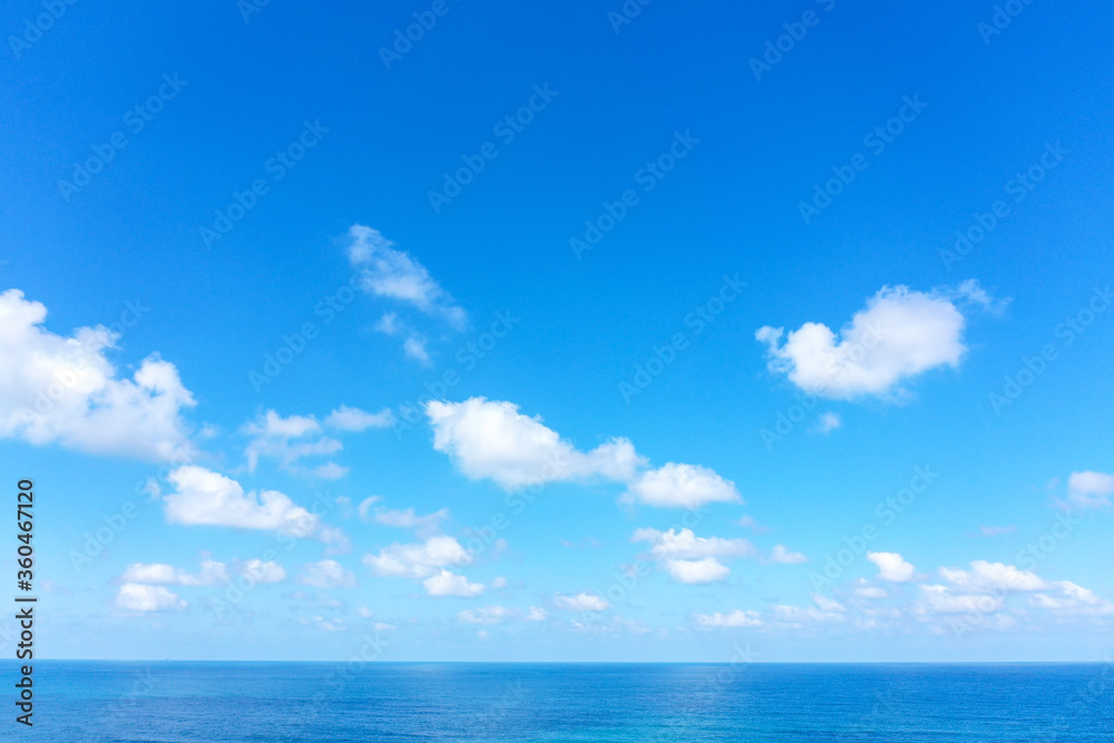 Aerial view of clear Ocean water with blue cloudy sky.
