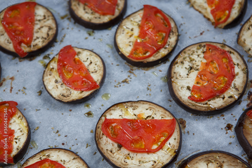 isolated filled frame close up shot of baked sliced aubergine eggplant with thin tomato slices on top, sprinkled with dry green basil and oregano herbs, lying on a white baking paper background isolated filled frame close up shot of baked sliced aubergine eggplant with thin tomato slices on top, sprinkled with dry green basil and oregano herbs, lying on a white baking paper background